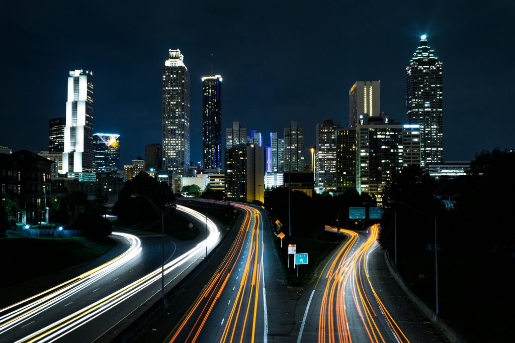 A vibrant cityscape at night showcasing light trails on the highway beneath towering skyscrapers.